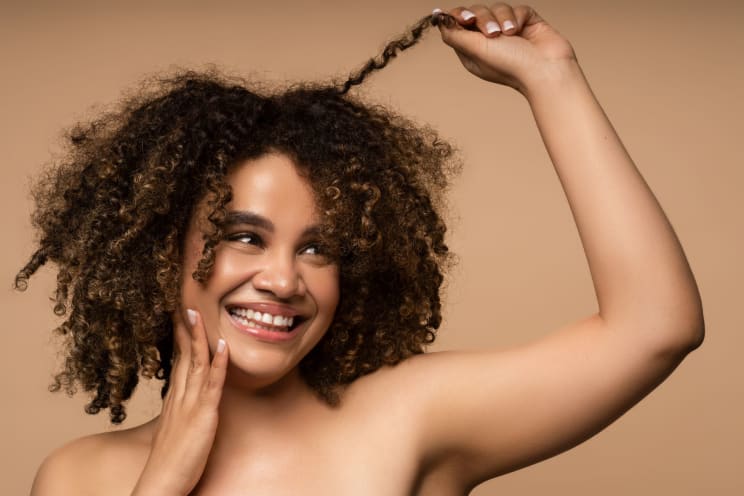 A Woman With Curly Hair, Smiling As She Pulls At A Lock Of Her Hair