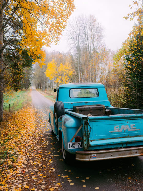 Vintage Turquoise GMC Truck Parked On A Leaf-covered Road Lined With Autumn Trees