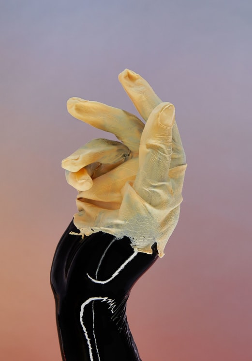 A Black Mannequin Hand, Wrapped In A Wrinkled Light Glove, Is Posed Gracefully Against A Pastel Background