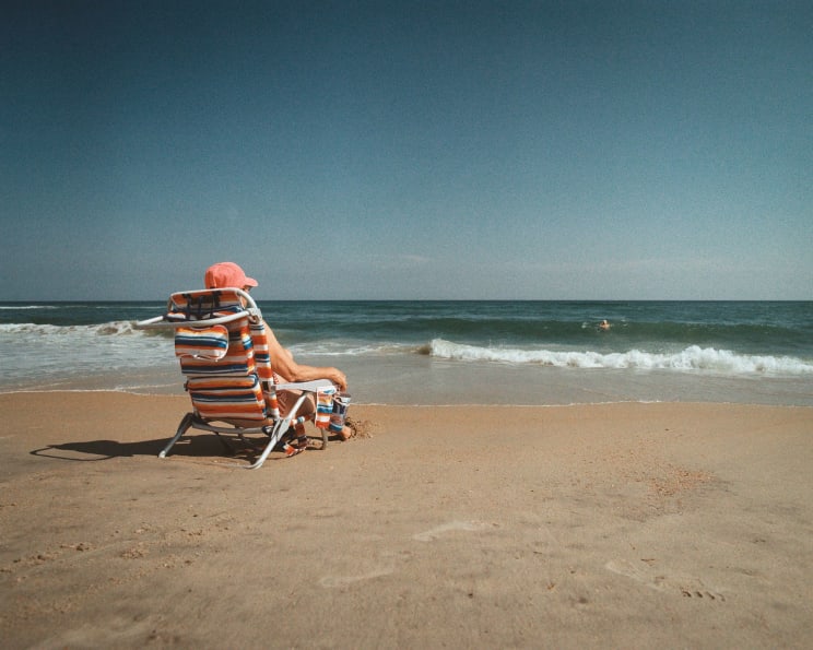 A Woman Wearing A Pink Hat Is Sitting In A Striped Beach Chair Watching The Sea