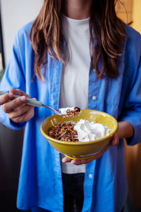 Woman Holding A Yellow Bowl With Granola And Whipped Cream