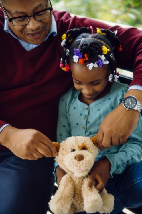 Father Sitting Next To His Daughter Who Is Holding A Teddy Bear