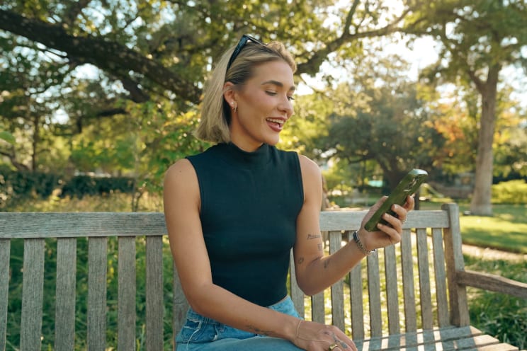 Woman Sitting On A Bench Smiles As She Holds Her Phone