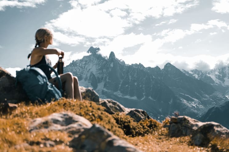 Woman Hiker Sitting On A Mountain As She Opens Her Thermos Bottle And Looks At Mountains In The Distance