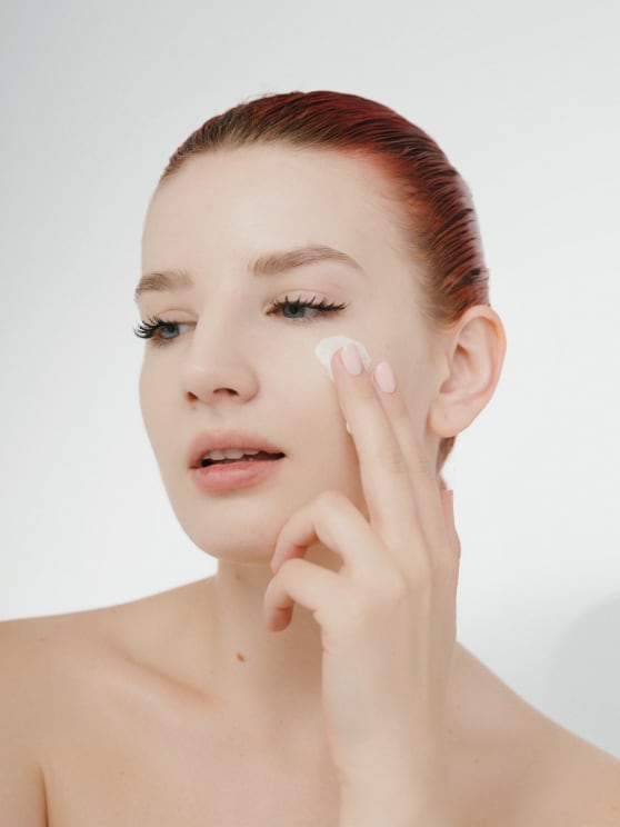 Woman Turns Her Head As She Rubs Skin Cream On Her Cheek With Her Fingers