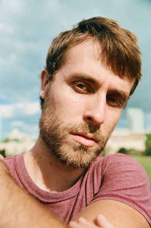 Close-up Of A Man Wearing A Burgundy T-shirt, Against An Outdoor Background