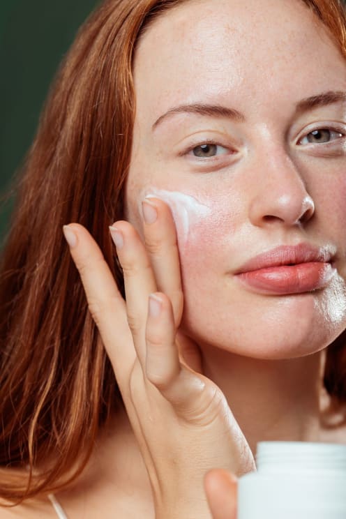 Red-haired Woman Applying White Cream To Her Face
