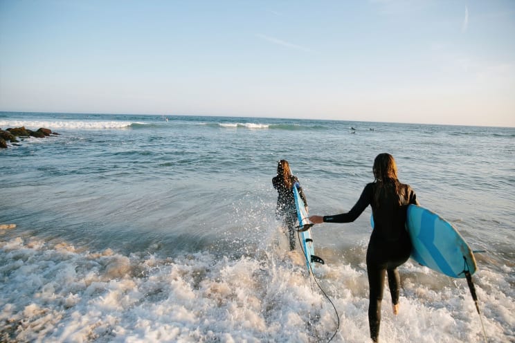 Two Women Entering The Sea With Surfboards