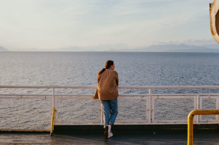 Woman Stands On The Deck Of A Ship Near The Coast Looking At The Water