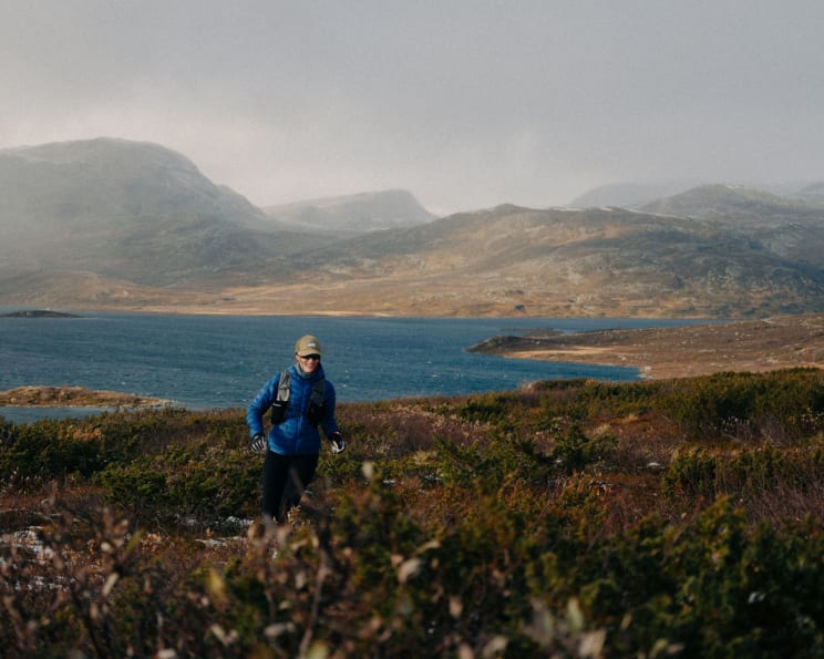 A Woman Hiking Through Grasslands Around A Lake With Mountains In The Distance
