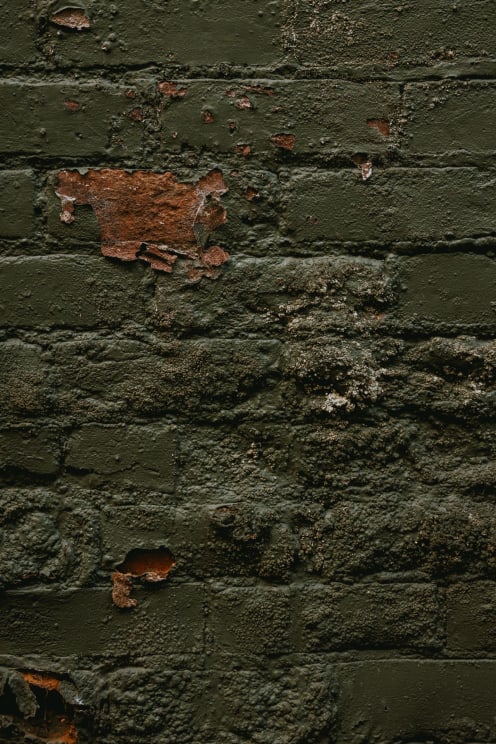 An Old Brick Wall Covered In Bubbling And Peeling Olive Green Paint