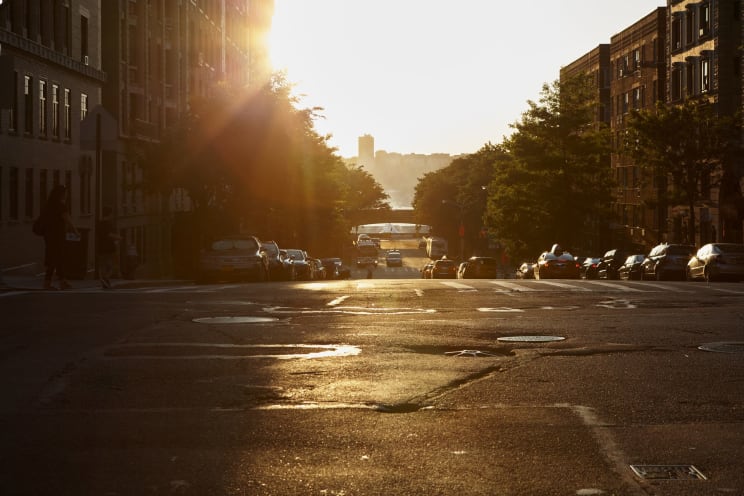 Several Vehicles Line The Street Of An Urban Neighborhood As The Sun Shines Brightly In The Sky