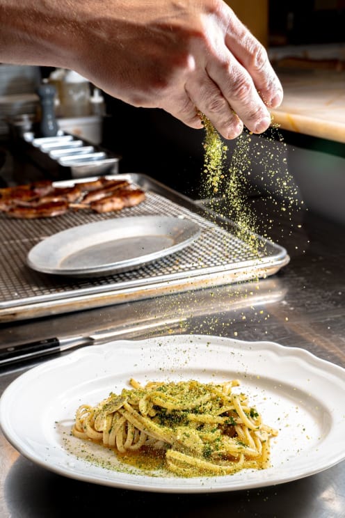 Hand Sprinkling A Green Herb Over A Plate Of Pasta