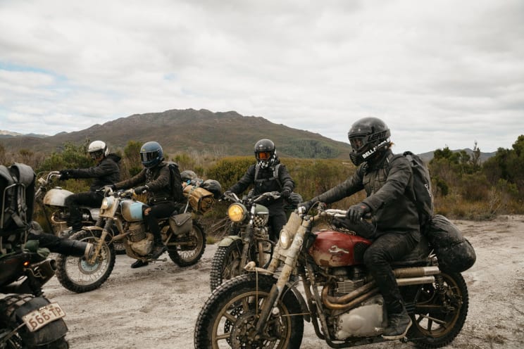 A Group Of Motorcycle Riders Are Parked On A Gravel Road In A Mountainous Area