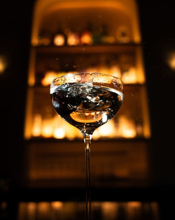 A Close-up Of A Cocktail Glass With A Vibrant, Warm-lit Bar Background