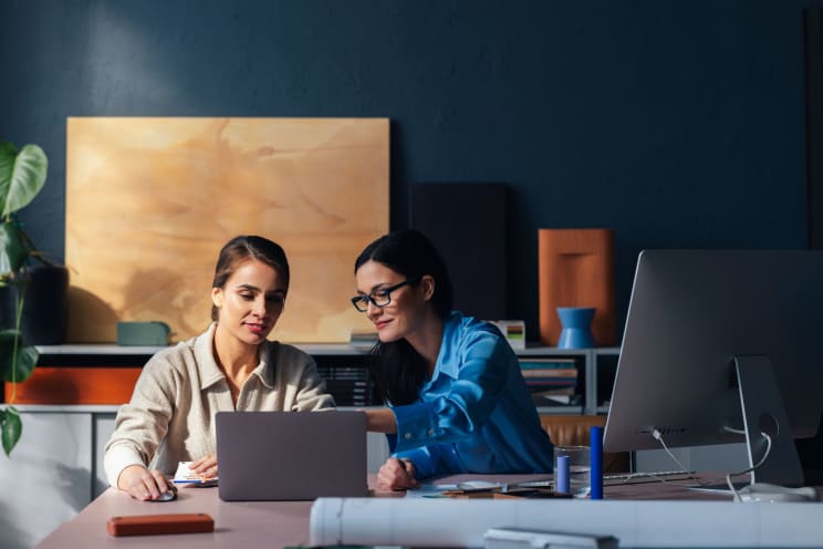 Two Women Sitting At An Office Desk Working On A Laptop