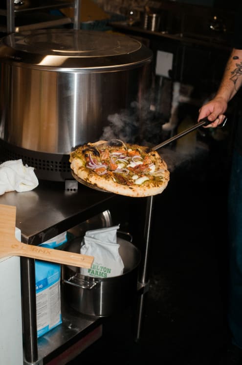 A Restaurant Employee Holds A Hot Pizza On A Long, Metal Peel