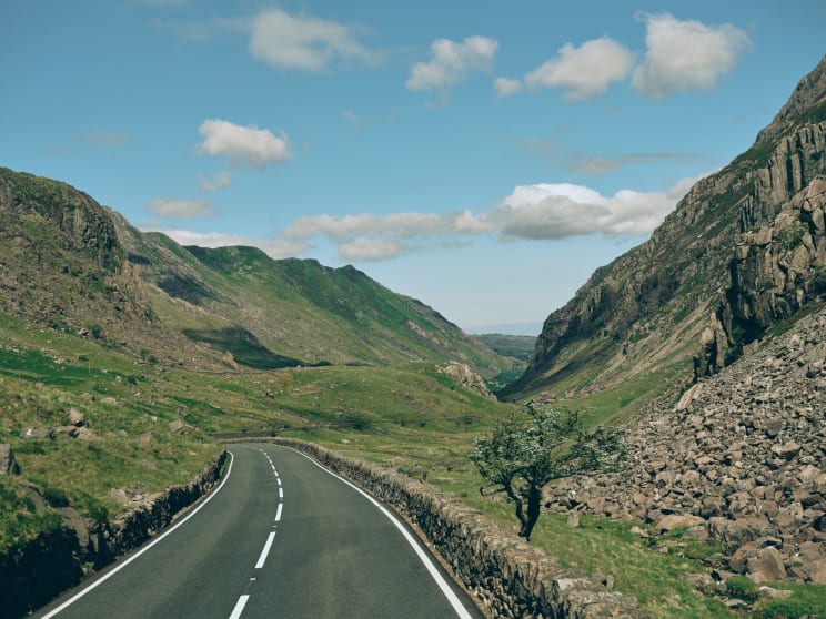 A Winding Road Through A Mountain Valley With Green, Rocky Slopes Under A Blue Sky