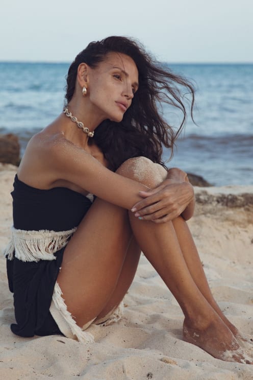 Woman Sitting On The Beach With Her Arms Wrapped Around Her Knees As The Wind Blows Her Hair