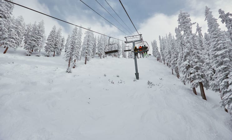 Three People Going On A Chairlift Up A Snowy Mountain