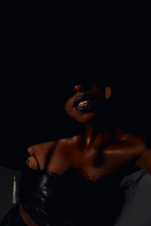 Details Of A Woman's Face, Lips With Dark Glossy Lipstick And Shoulders Are Illuminated Against A Predominantly Dark Background