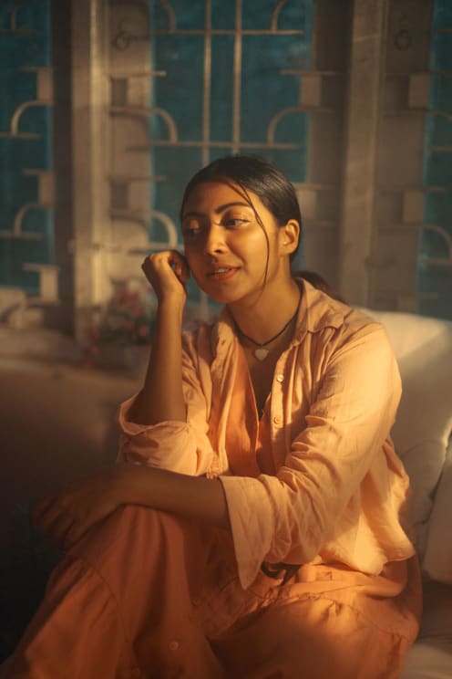 A Woman In Peach Colored Clothes Sitting On A White Couch