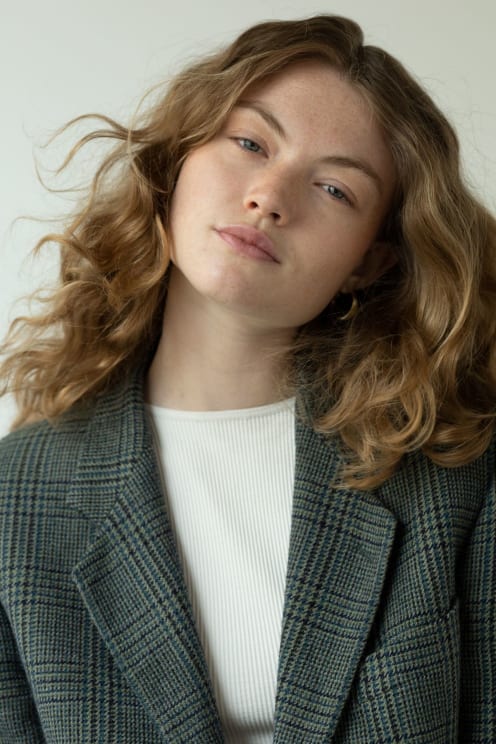 Woman Wearing A Blazer Tilts Her Head As She Looks Into The Camera