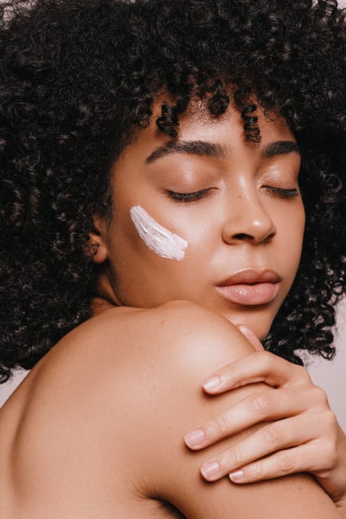 Woman With Skin Cream On Her Cheek Turns Her Head And Holds Her Arm