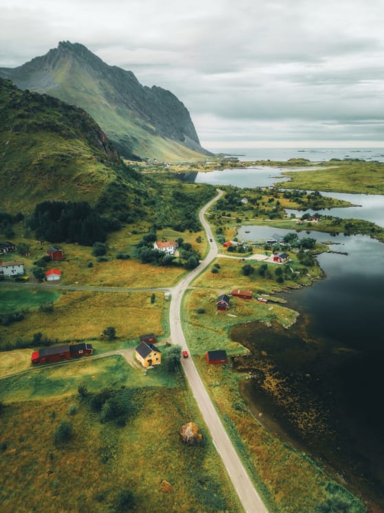 A Winding Road Runs Through A Picturesque Village Surrounded By Mountains And Lakes