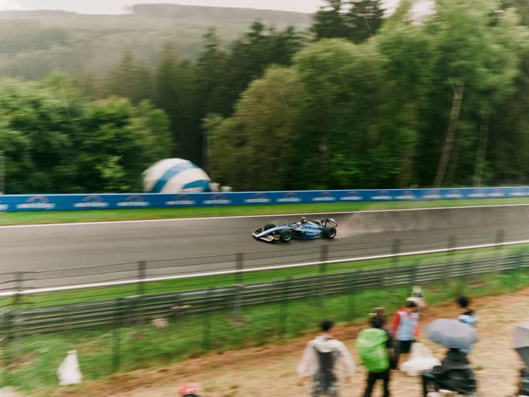 A Crowd Watches As A Race Car Drives By On An Outdoor Track
