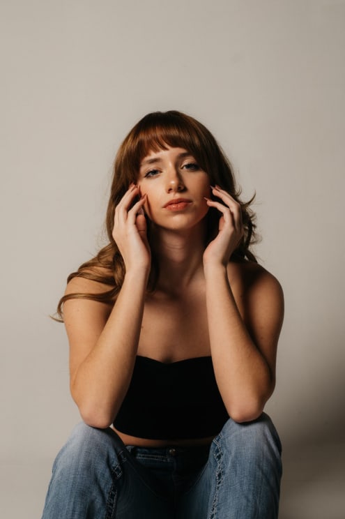Woman Sitting With Her Hands On The Sides Of Her Face As She Looks Into The Camera