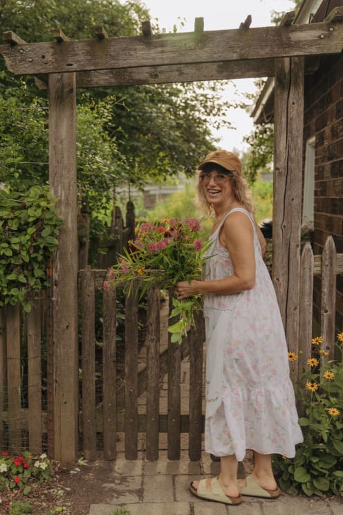 Woman Outside Of Her House Along The Coast Holding A Bouquet Of Flowers As She Turns And Smiles