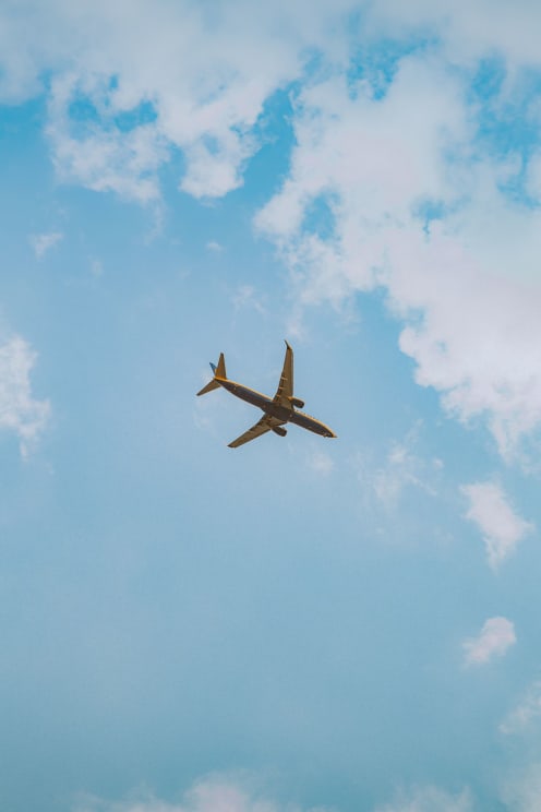 A Commercial Airplane Flies Through A Bright Blue Sky Dotted With White Clouds