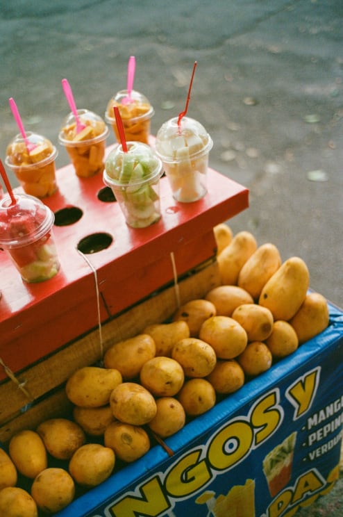 Street Cart With Exposed Mangoes And Plastic Cups Containing Cut Fruit, Accompanied By Colorful Forks