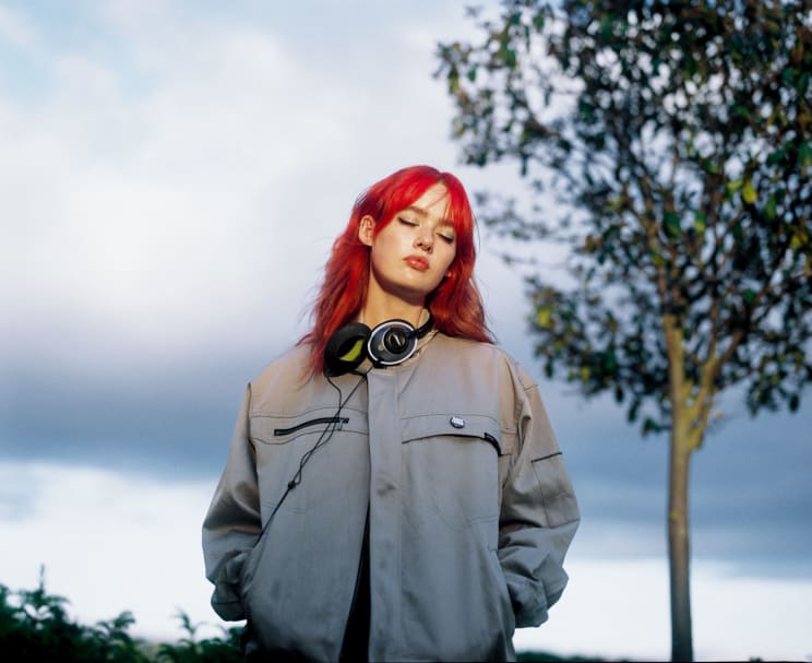 A Woman With Unnaturally Red Hair Wearing Headphones Around Her Neck