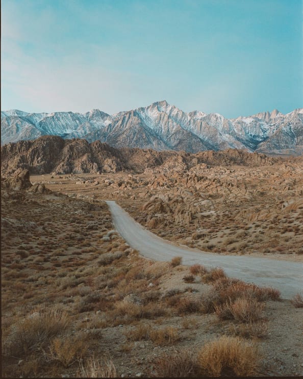 A Dirt Road Winds Through Desert Scrub Toward Snowy Mountains