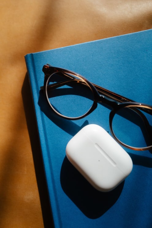 A Pair Of Glasses And An Earphone Case On A Blue Book