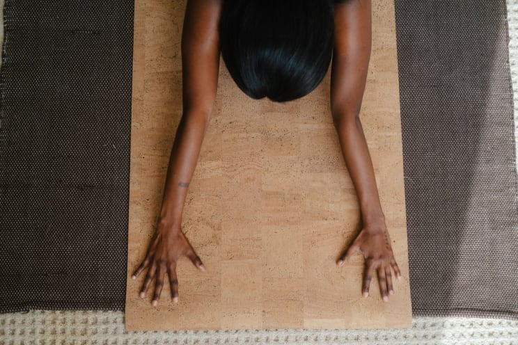 A Black Woman Performs Stretches On A Tan Yoga Mat