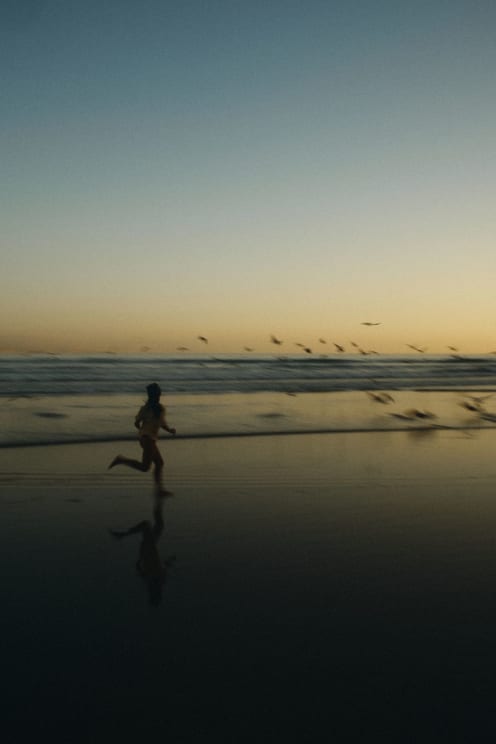 Silhouette Of A Young Woman Running Across Wet Sand At Dawn