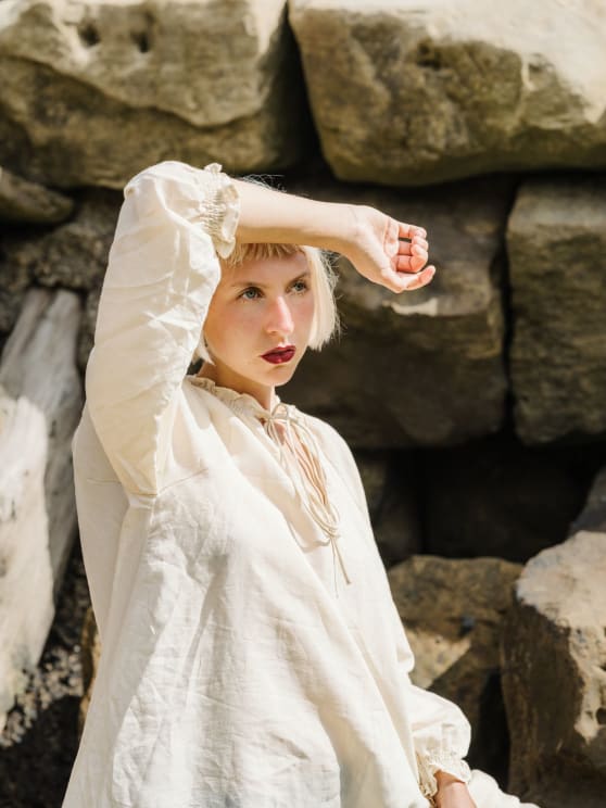 A Woman In A White Dress Poses With Her Arm Up To Her Forehead