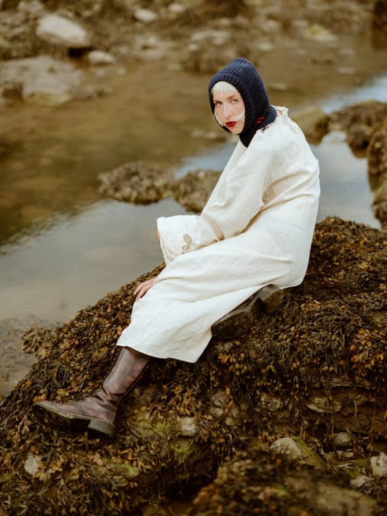 Woman In A Dark Blue Cap Sitting On A Rock By A Stream Wearing A White Dress