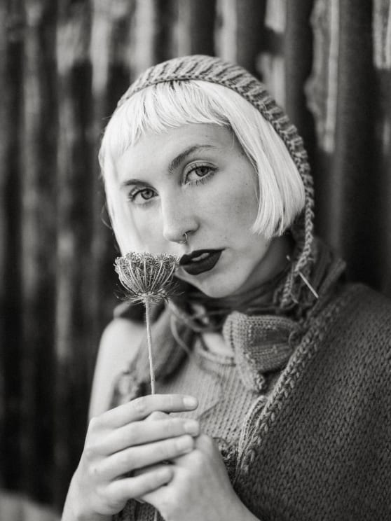 Portrait Of A Woman With A Cap Holding A Flower Close To Her Face