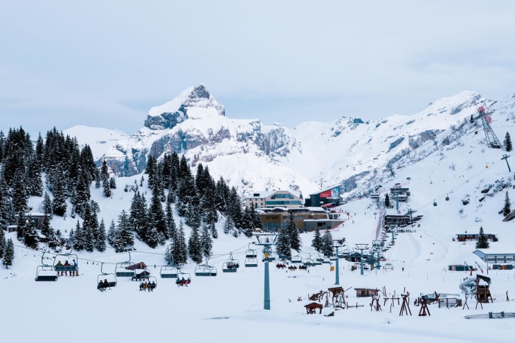 A Ski Resort Surrounded By Snow-capped Mountains And Cable Cars Carrying Skiers