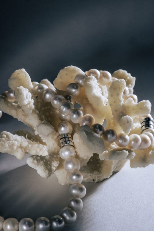 Strand Of Pearl Beads With Silver Accents Draped Over A Textured White Coral Piece, Set Against A Dark Background