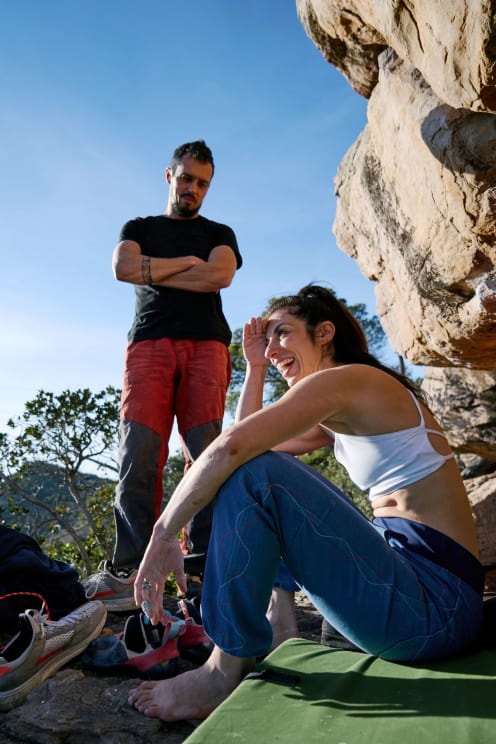A Couple Of Climbers Rest Outdoors Among The Rocks, The Woman Smiling While The Man Looks On With His Arms Crossed