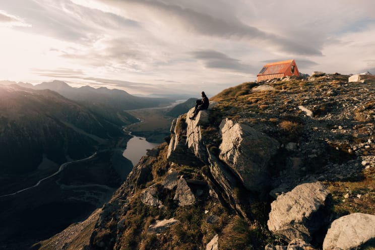 A Person Sitting On A Rocky Mountain During The Day