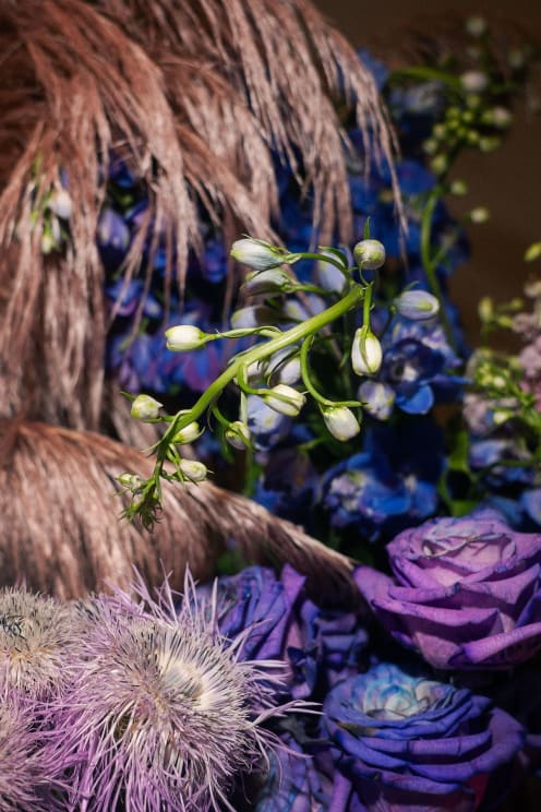 A Flower Arrangement With Blue And Purple Flowers And Copper Pampas Grass