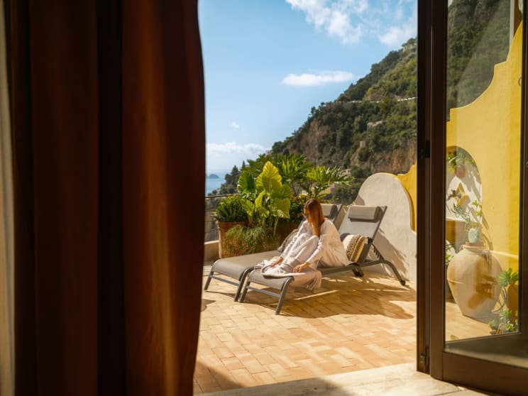 A Young Woman Sits In A Chaise Lounge On A Balcony In A Coastal Destination Location