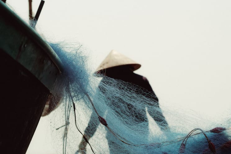 A Traditional Hat Fisherman Handles Nets Next To A Boat