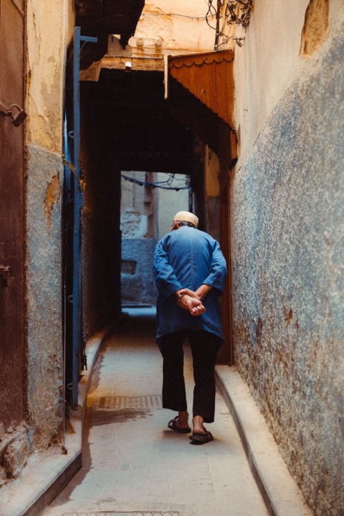 An Elderly Man Walks Hunched Over Through The Alleyway